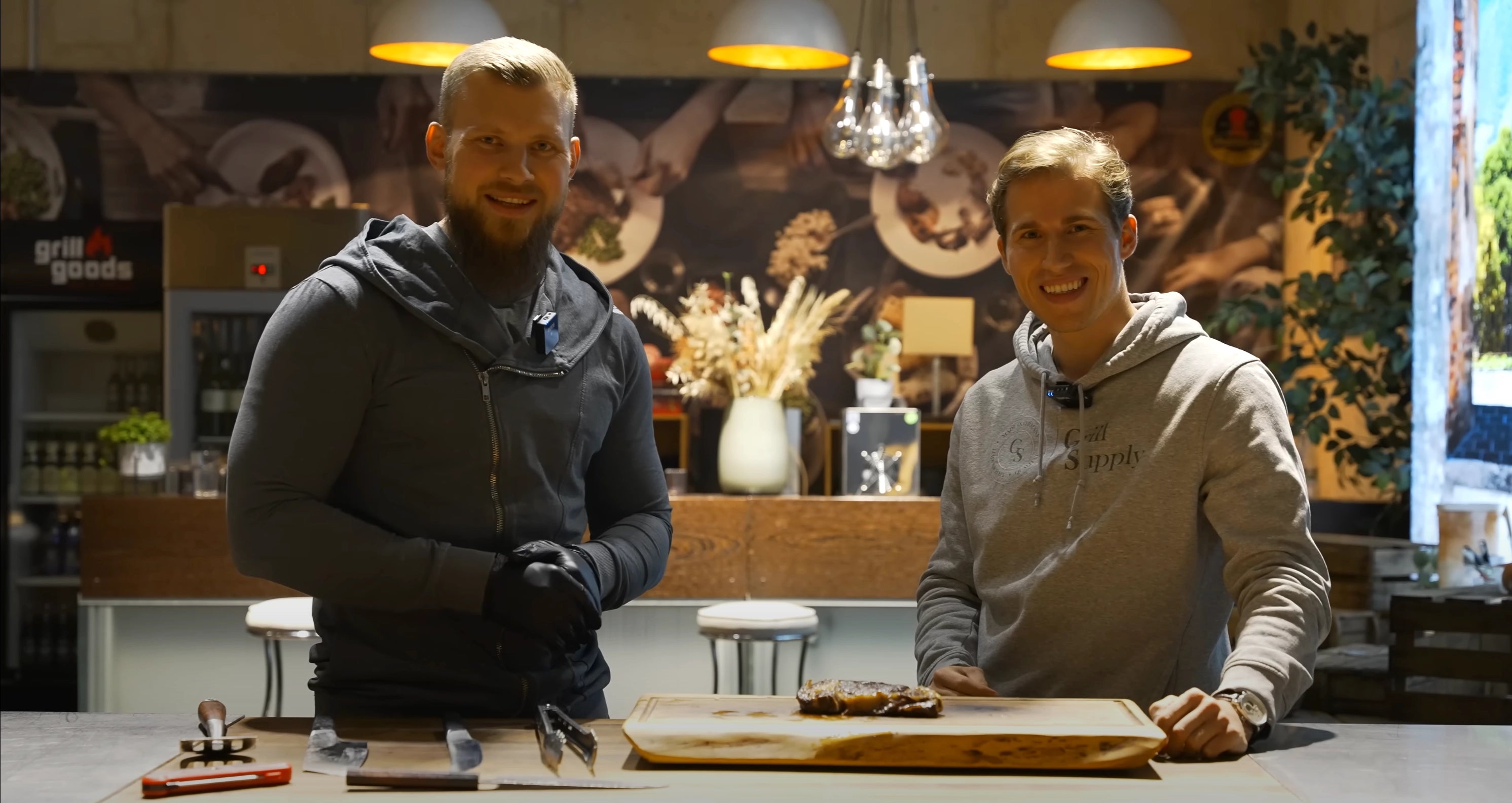 Joscha und Daniel stehen im Seminarraum von Grillgoods und ein Steak liegt vor ihnen.